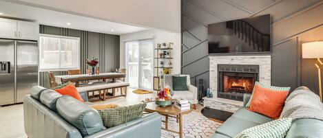 A modern living room with a fireplace, grey sofas, and a dining area with a table and chairs.