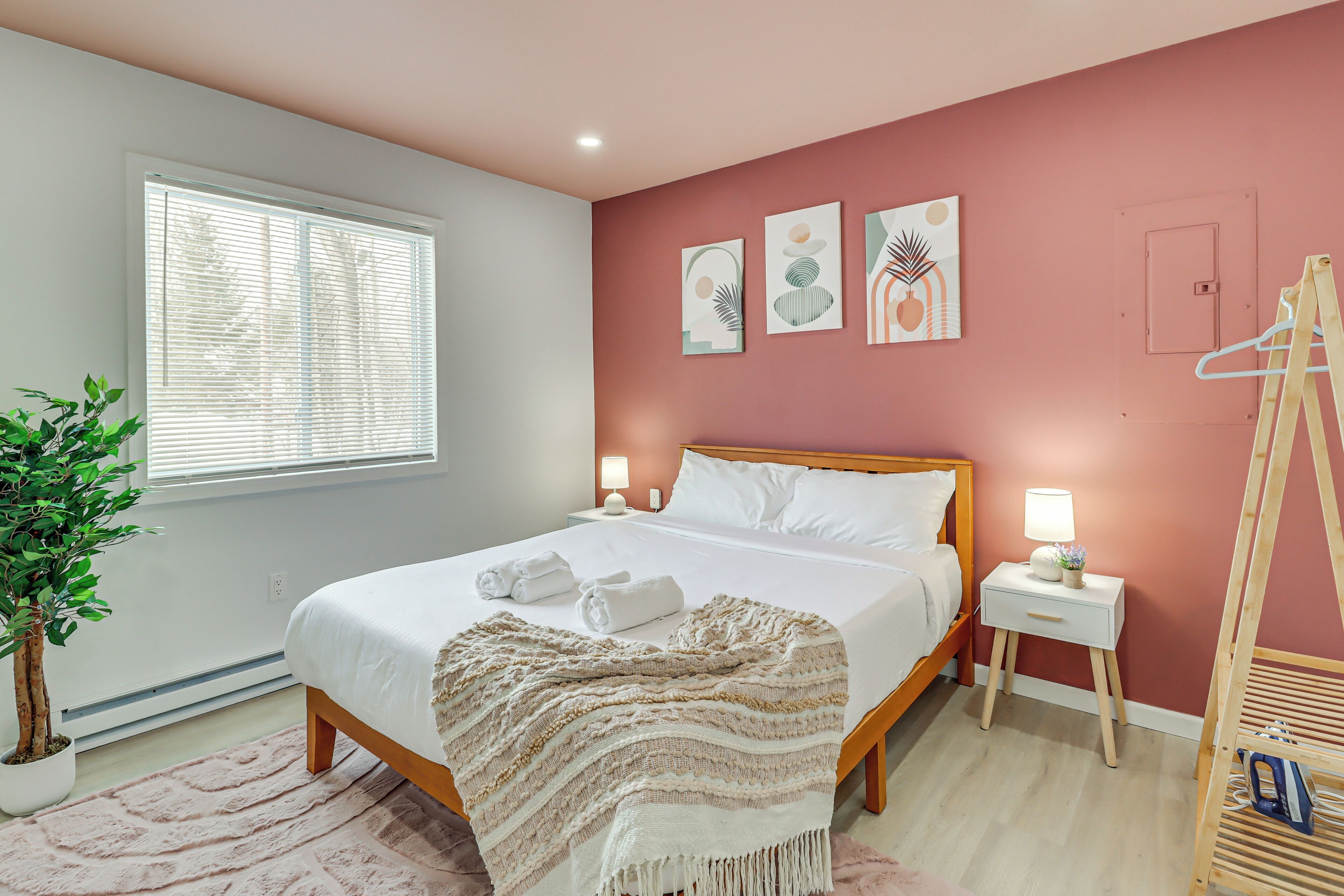 A bedroom with a bed, bedside tables, a bedside lamp, a hanging plant, and artwork on the wall.