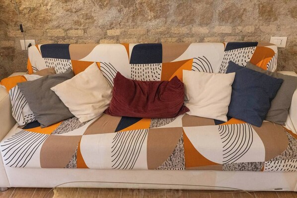 A sofa with a geometric patterned fabric, a red cushion, and a white cushion. - Rooms Steps from Colosseum by Welcome In (Rome)