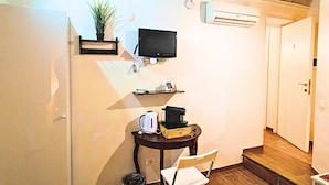 A room with a flat-screen TV mounted on the wall, a small table with a coffee maker and a plant, and an air conditioning unit. - Rooms Steps from Colosseum by Welcome In (Rome)