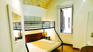 A room with bunk beds, a desk, a chair, a window with a view of buildings, and a wooden floor. - Rooms Steps from Colosseum by Welcome In (Rome)