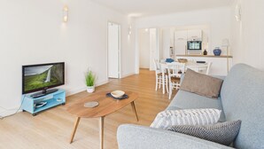Una sala de estar moderna con una televisión de pantalla plana, un sofá, una mesa de centro y un comedor con una cocina al fondo.