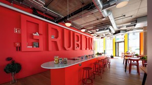 Ein modernes Interieur mit einer auffälligen roten Wand, einer Bar mit Hockern und einer Sitzgruppe mit Tischen und Stühlen.