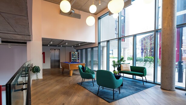 Eine geräumige Lobby mit Billardtisch, grünen Stühlen und einem großen Fenster mit Blick nach draußen.