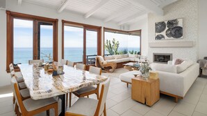 A spacious living area with a large dining table, comfortable seating, a fireplace, and a view of the ocean. - Private Bluff-Top Oceanfront Estate | Beach Access (Encinitas)