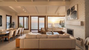A spacious living area with a large sofa, dining table, and chairs, a fireplace, and a view of the sea. - Private Bluff-Top Oceanfront Estate | Beach Access (Encinitas)