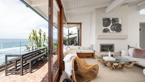 A spacious living area with a large glass door leading to a balcony overlooking the ocean, furnished with a sofa, a coffee table, and a wicker chair. - Private Bluff-Top Oceanfront Estate | Beach Access (Encinitas)