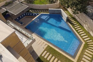 A swimming pool with a geometric shape, surrounded by a concrete deck and a small grassy area. - ALSAWAH Grand Palace at Sheikh Zayed - 6BR, Pool & Private Garden (6th of October City)