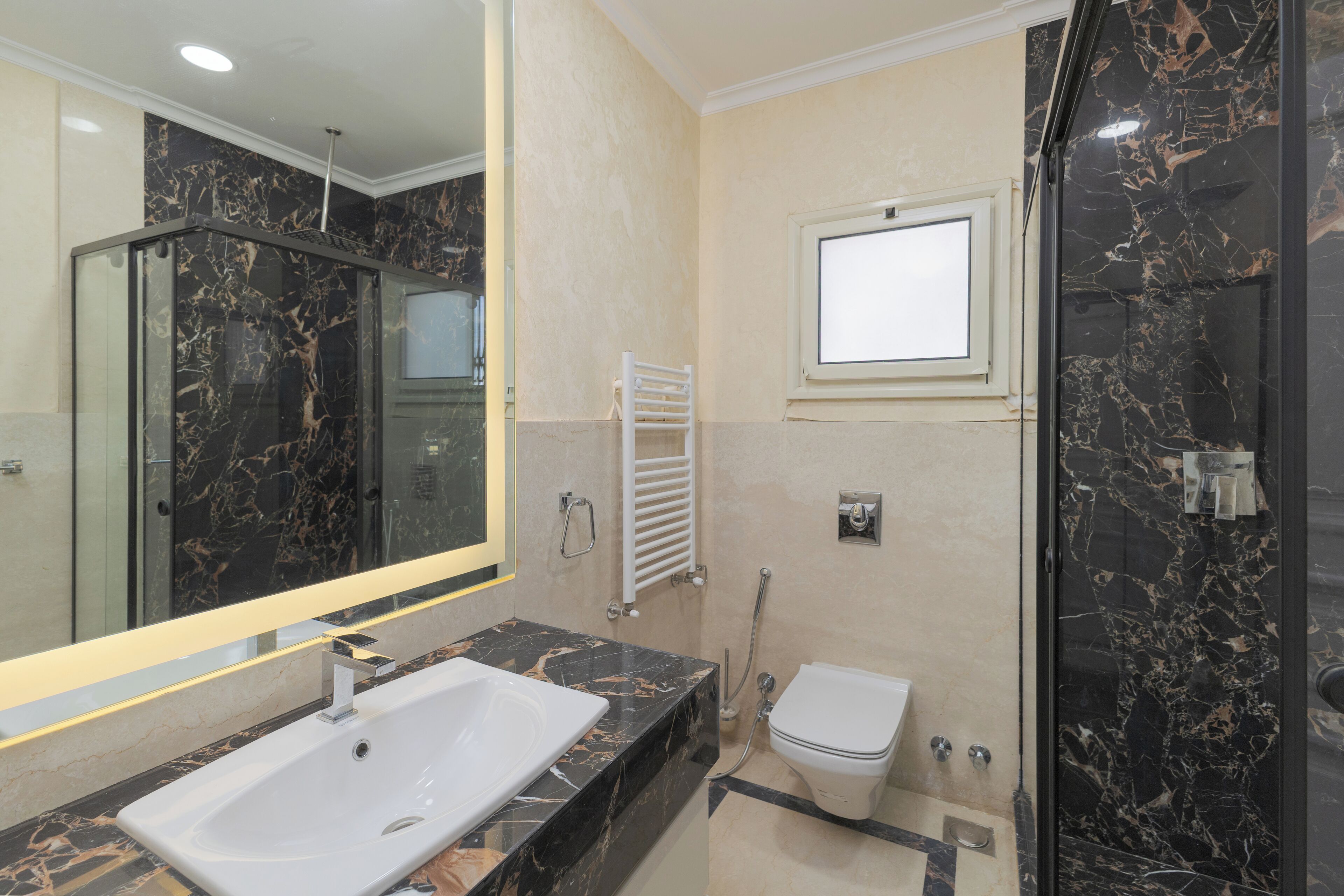A modern bathroom with a marble sink, a glass shower enclosure, and a toilet.
