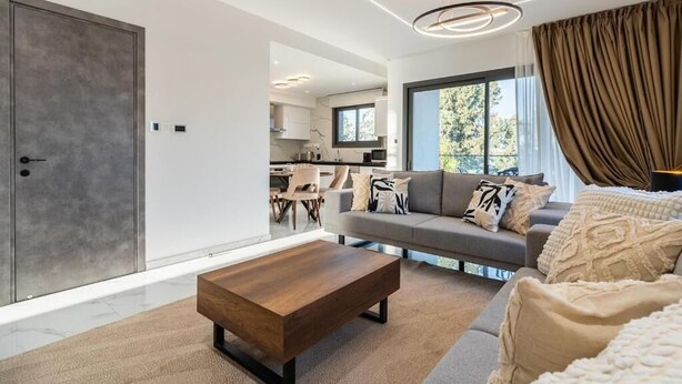 A modern living room with a sofa, coffee table, and a view of the kitchen. - Casino & Mall Luxury Penthouse Suite (Limassol)