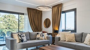 A modern living room with two grey sofas, a wooden coffee table, and a large window with curtains. - Casino & Mall Luxury Penthouse Suite (Limassol)