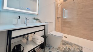 A modern bathroom with a white sink, a large mirror, a shower, and a toilet. - Sorolla Urban Suites (Valencia)