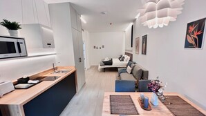 A modern kitchen with a microwave, sink, and wooden countertop. There is a dining area with a table, chairs, and a vase of flowers. - Sorolla Urban Suites (Valencia)