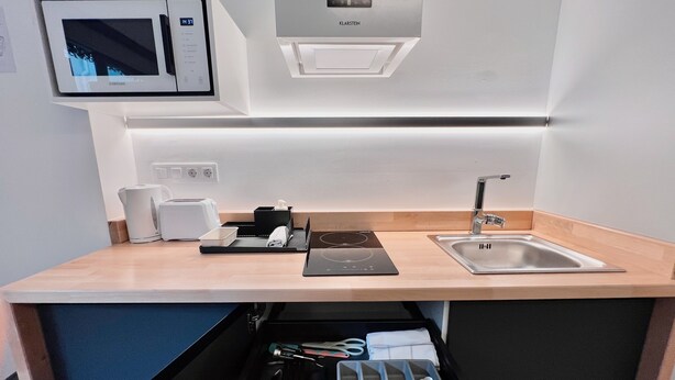 A modern kitchen with a microwave, toaster, sink, and a drawer with utensils. - Sorolla Urban Suites (Valencia)