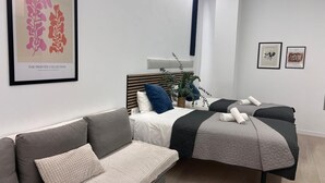 A modern bedroom with a bed, two bedside tables, a sofa, and a framed artwork on the wall. - Sorolla Urban Suites (Valencia)