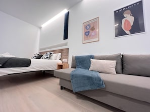 A modern bedroom with a bed, a sofa, and two wall art pieces. - Sorolla Urban Suites (Valencia)