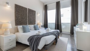 Ein modernes Schlafzimmer mit einem großen Bett, Nachttischlampen, einem Nachttisch, einer Kommode und Blick ins Freie.