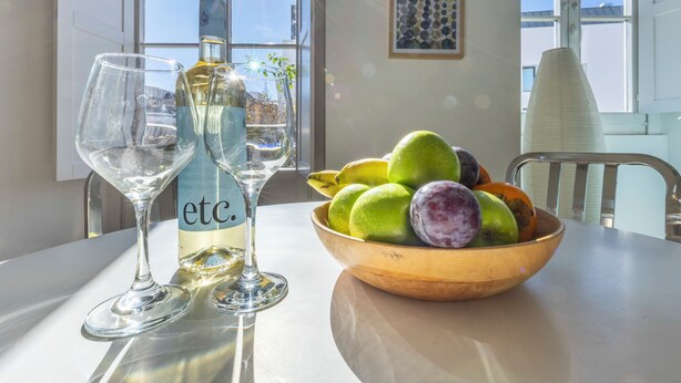 Ein Tisch mit einer Weinflasche, zwei Weingläsern und einer Obstschale.