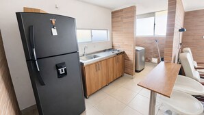 Une cuisine moderne avec un réfrigérateur noir, des armoires en bois, un évier en acier inoxydable et un coin repas comprenant une table en bois et des chaises blanches.