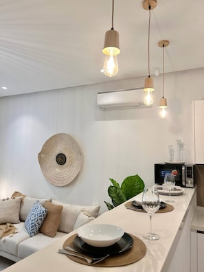 A modern kitchen with a central island, pendant lighting, an air conditioning unit, and a decorative wall hanging. - La Bohème Signature Apartment in La Marsa (La Marsa)