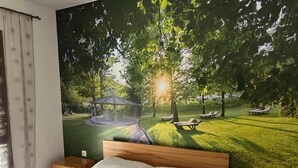 A bedroom with a large mural of a park scene, a wooden bed, and a nightstand. - Jazina Hotel (Jazina)