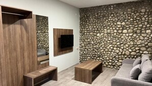 A modern living room with a stone wall, built-in wooden shelves, a flat-screen TV, and a grey sofa. - Jazina Hotel (Jazina)