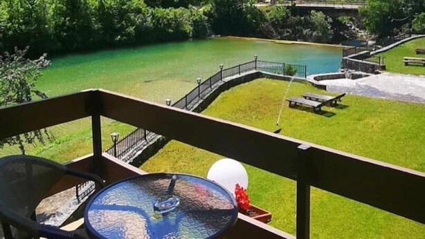 A balcony with a table and chairs overlooking a river and forested hills. - Jazina Hotel (Jazina)