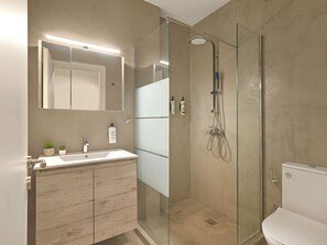 Ένα σύγχρονο μπάνιο με ένα ντους που διαχωρίζεται με γυάλινο διάφραγμα, έναν διπλό νιπτήρα και μια τουαλέτα.