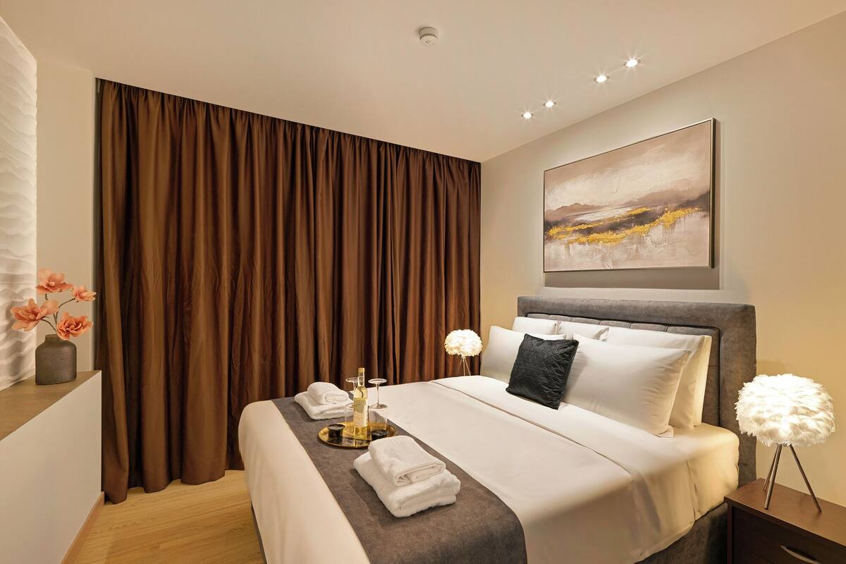 A modern hotel room with a large bed, a nightstand, a lamp, and a painting on the wall.