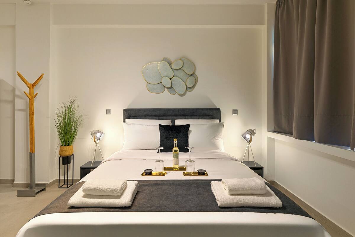 A modern bedroom with a large bed, a decorative wall piece, a coat rack, and a potted plant.