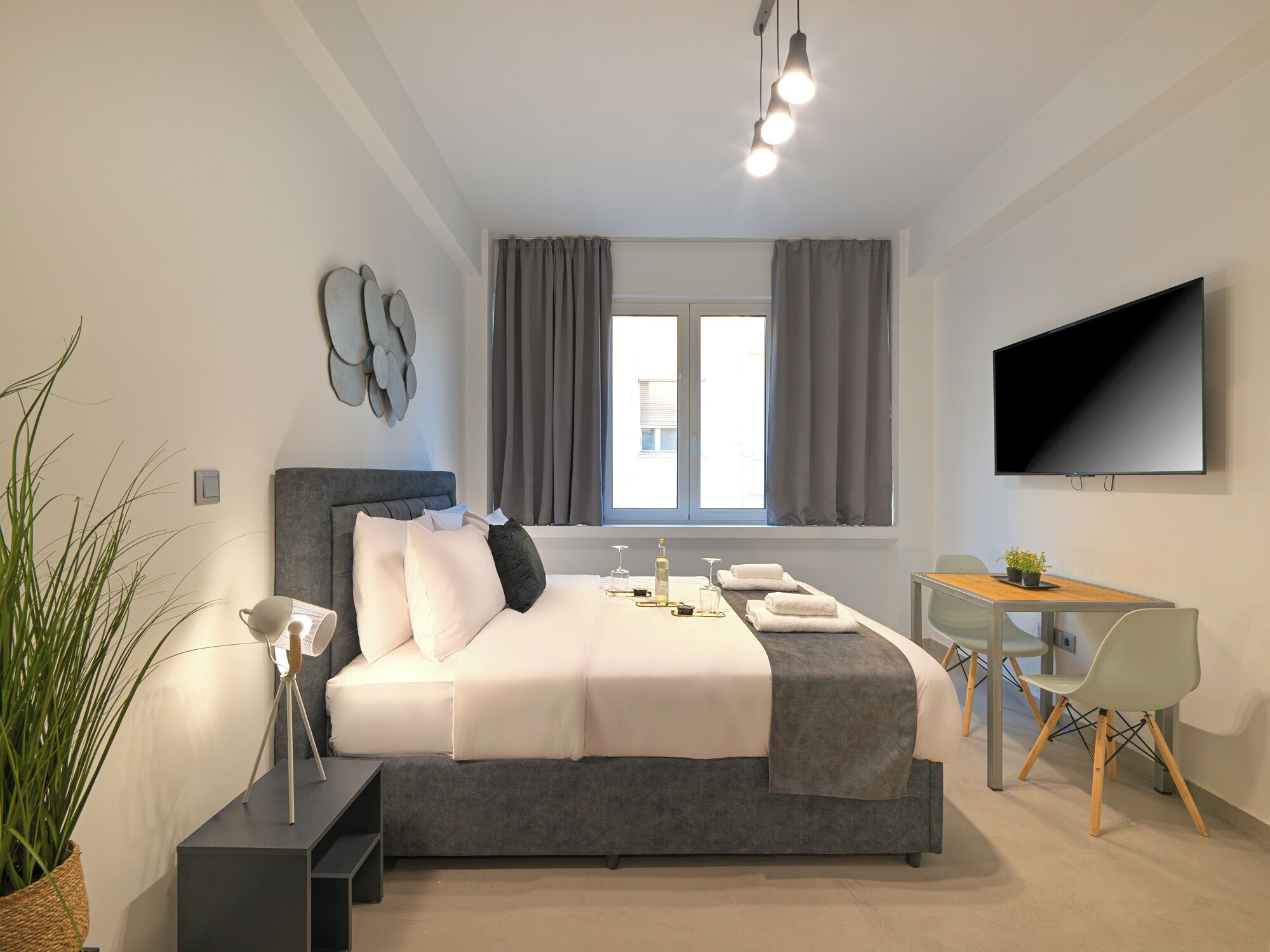 Un dormitorio moderno con cama, mesita de noche, lámpara, televisor y ventana con cortinas.