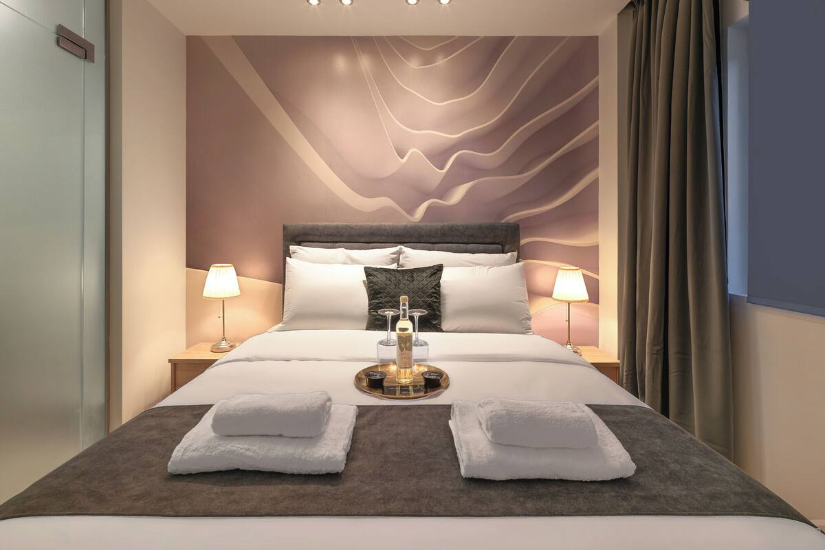 A modern hotel room with a large bed, two bedside lamps, a tray with toiletries, and a decorative wall.
