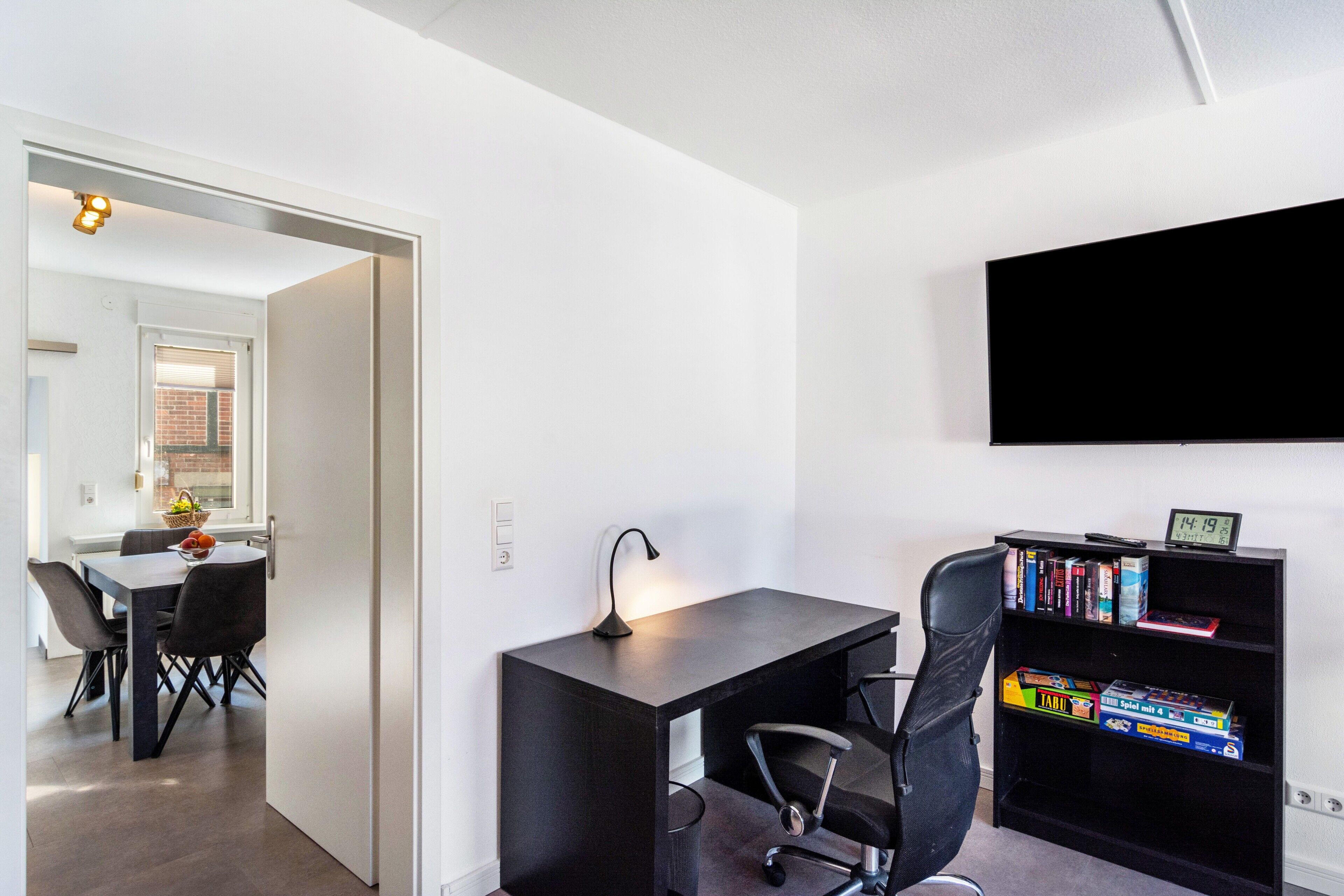 A modern room with a desk, chair, bookshelf, and a TV mounted on the wall.