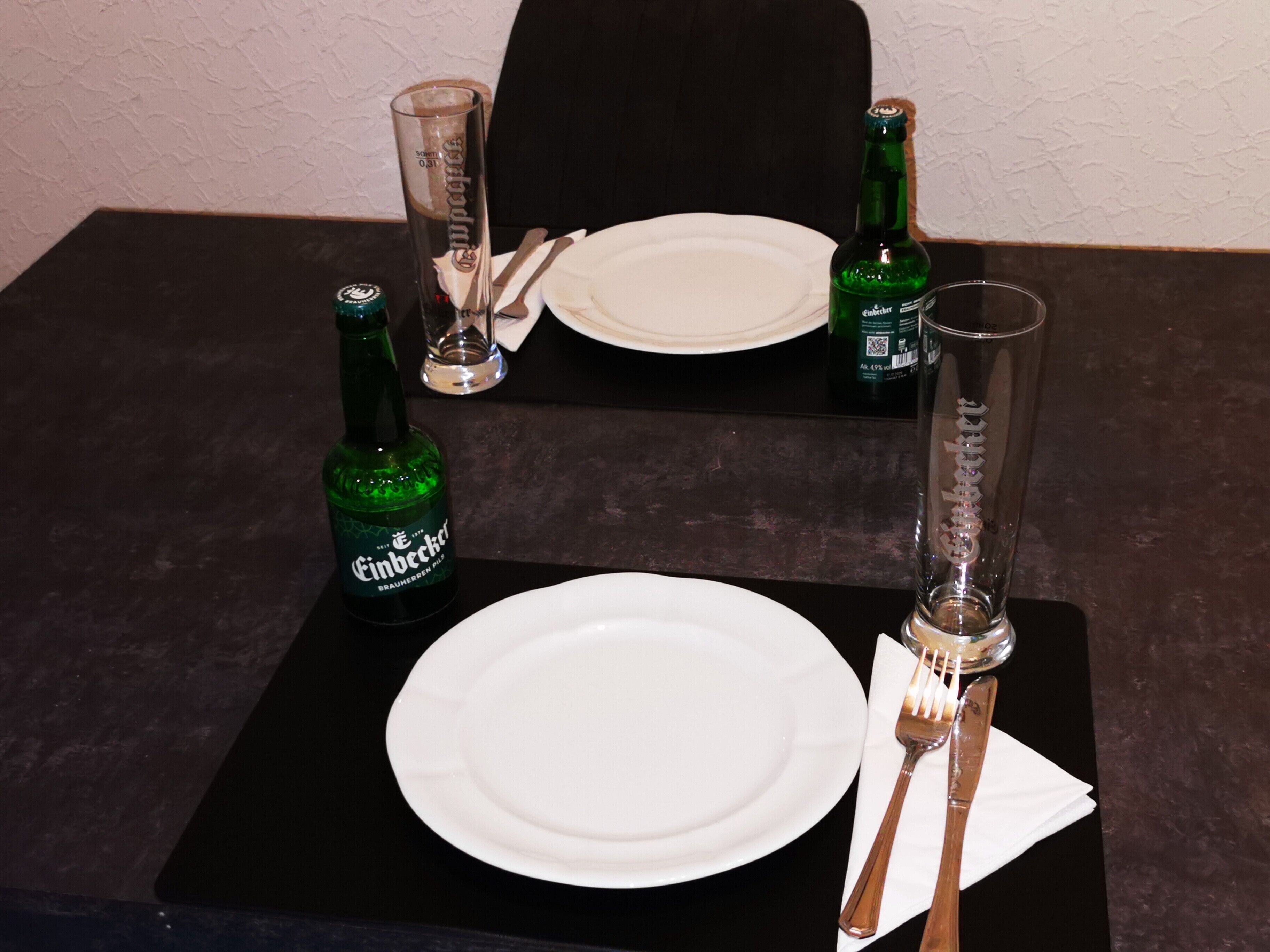 Taula preparada amb un plat blanc, dues forques, un ganivet, un got i dues ampolles de cervesa.