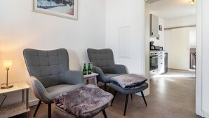 Un salon moderne avec deux fauteuils gris, une petite table sur laquelle sont posées des bouteilles et un tableau encadré accroché au mur.