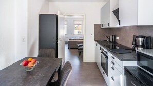 Une cuisine moderne avec un coin repas, un réfrigérateur, une machine à café et une vue sur la chambre adjacente.