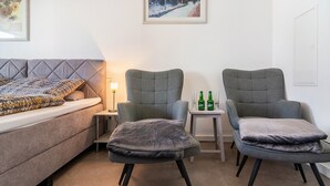 Une pièce comprenant un lit, deux fauteuils, une petite table avec des bouteilles et une lampe.
