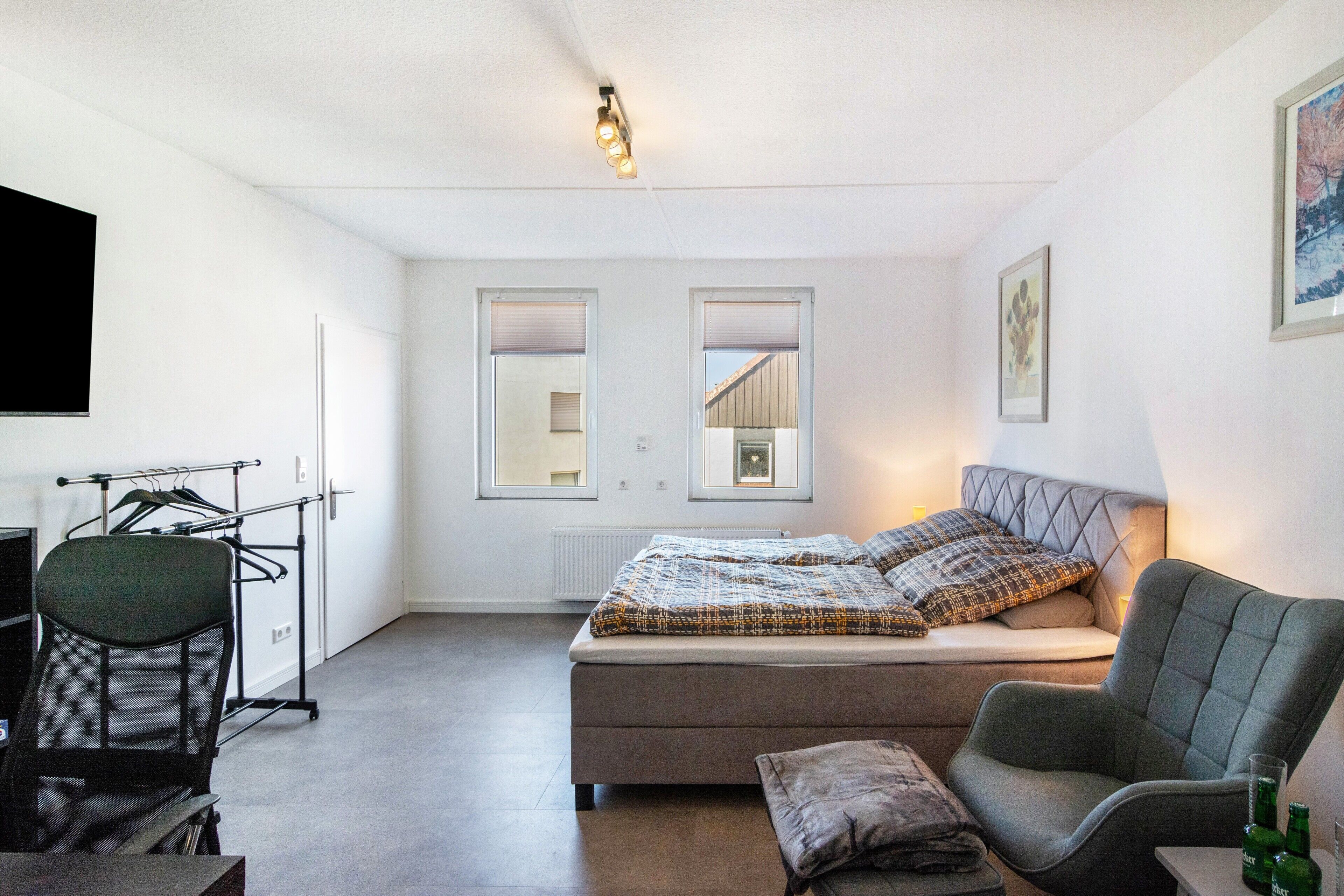A bedroom with a bed, a chair, a desk, and a radiator.