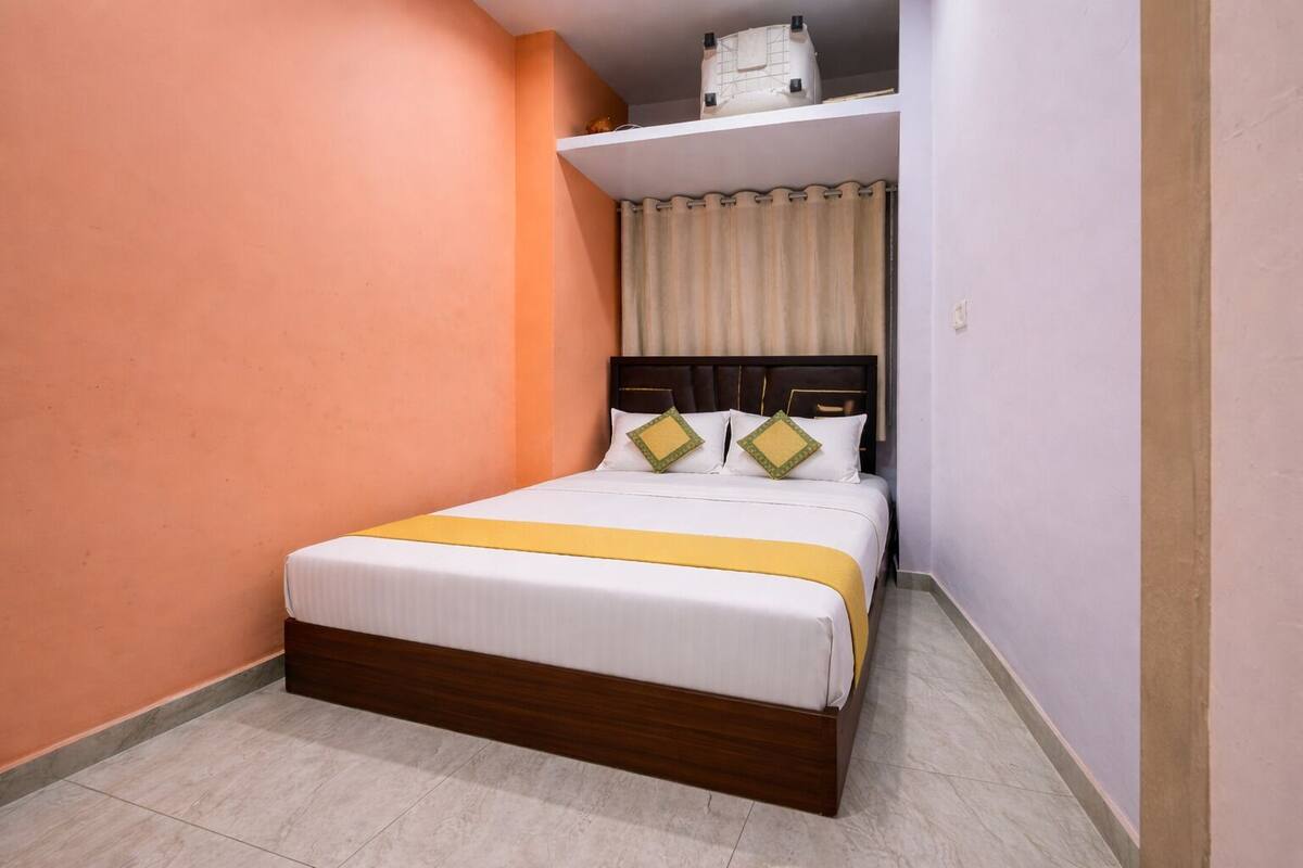 A single bed with a wooden frame, white bedding, and a yellow accent.