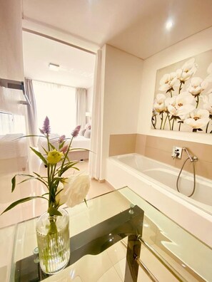 A modern bathroom with a glass-topped vanity, a bathtub, and a wall-mounted shower. - Sunset Views at Infinity Blouberg (Cape Town)
