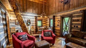 A log cabin interior with wooden walls, a dining area, and two red armchairs.