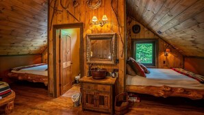 A rustic cabin with a loft bedroom, wooden walls, a wooden bench, a sink, and a window with a view of trees.