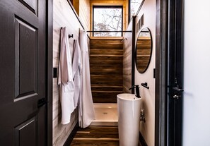 Een kleine badkamer met houten vloer, een witte wastafel en een raam boven de douche.