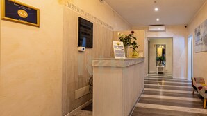 A hotel reception area with a reception desk, a framed guest review plaque, a signboard, and a hallway leading to the rooms. - SanremoInn Exclusive rooms (Sanremo)