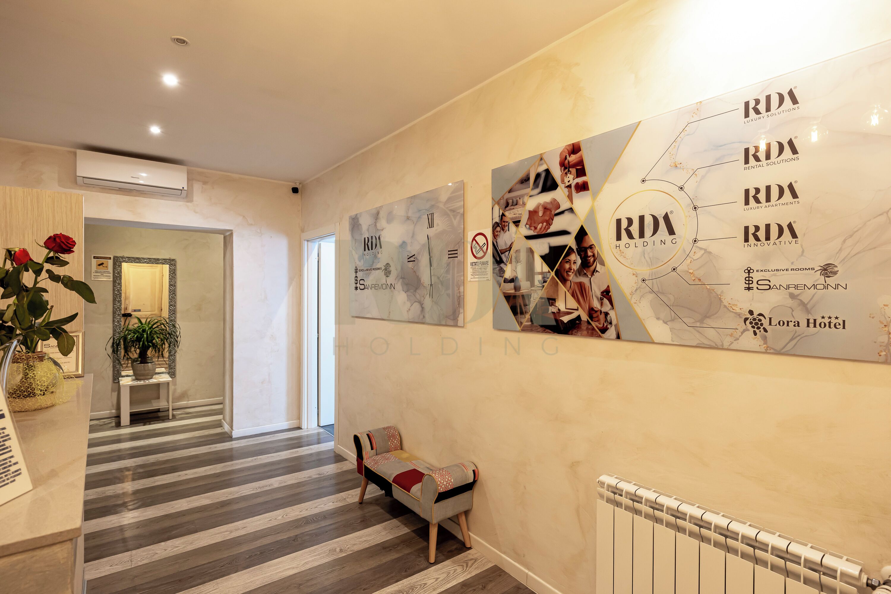 Un couloir d’hôtel avec un banc, un comptoir de réception et un mur orné du logo de RDA Holding.