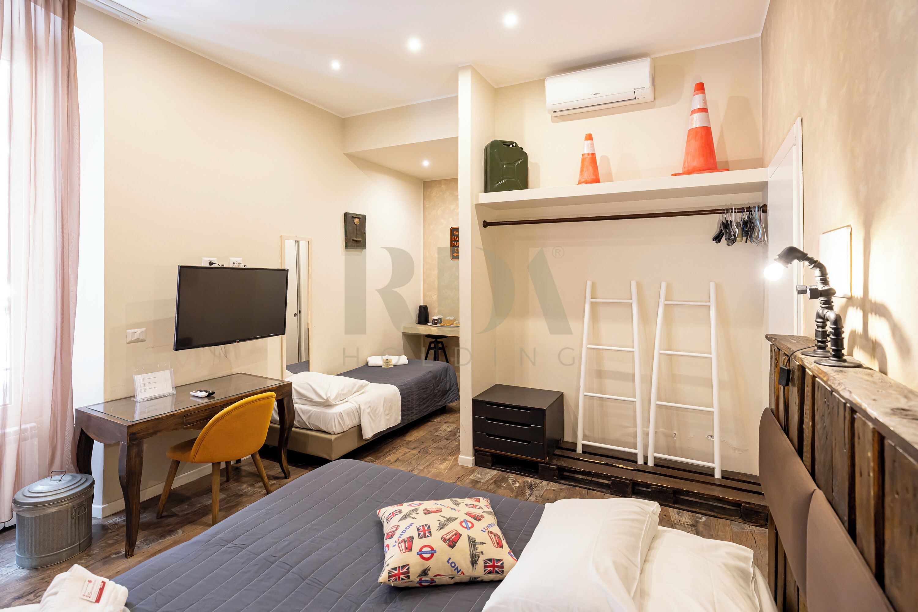 Une chambre d’hôtel comprenant un lit, un bureau avec un ordinateur, une chaise, une télévision, une armoire et une échelle.