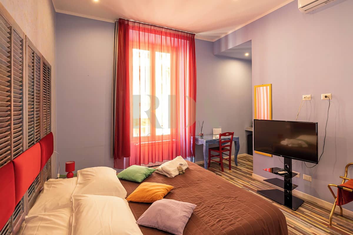 Une chambre d’hôtel équipée d’un lit, d’un bureau, d’une chaise, d’une télévision et d’une fenêtre avec des rideaux.
