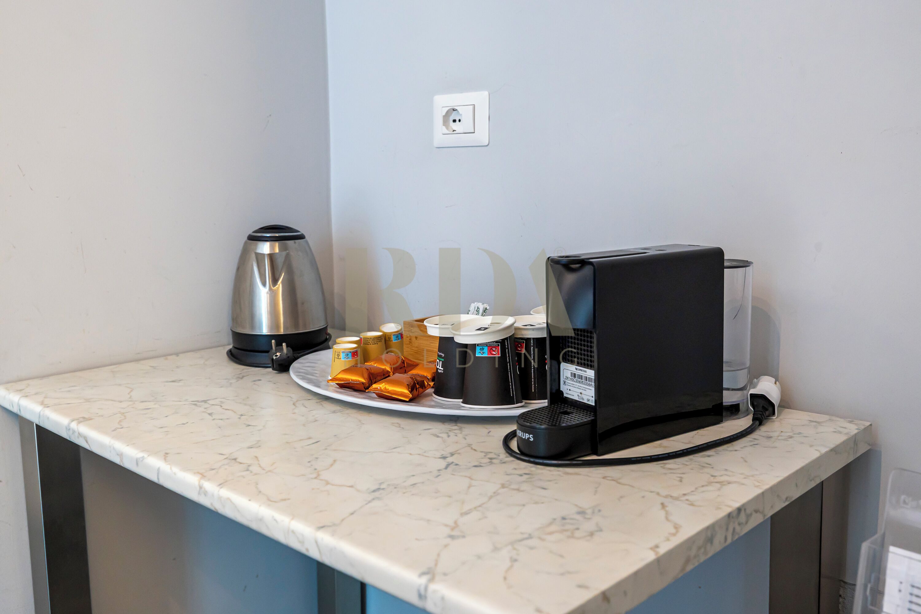 A kitchen counter with a coffee maker, a kettle, and a plate of food.