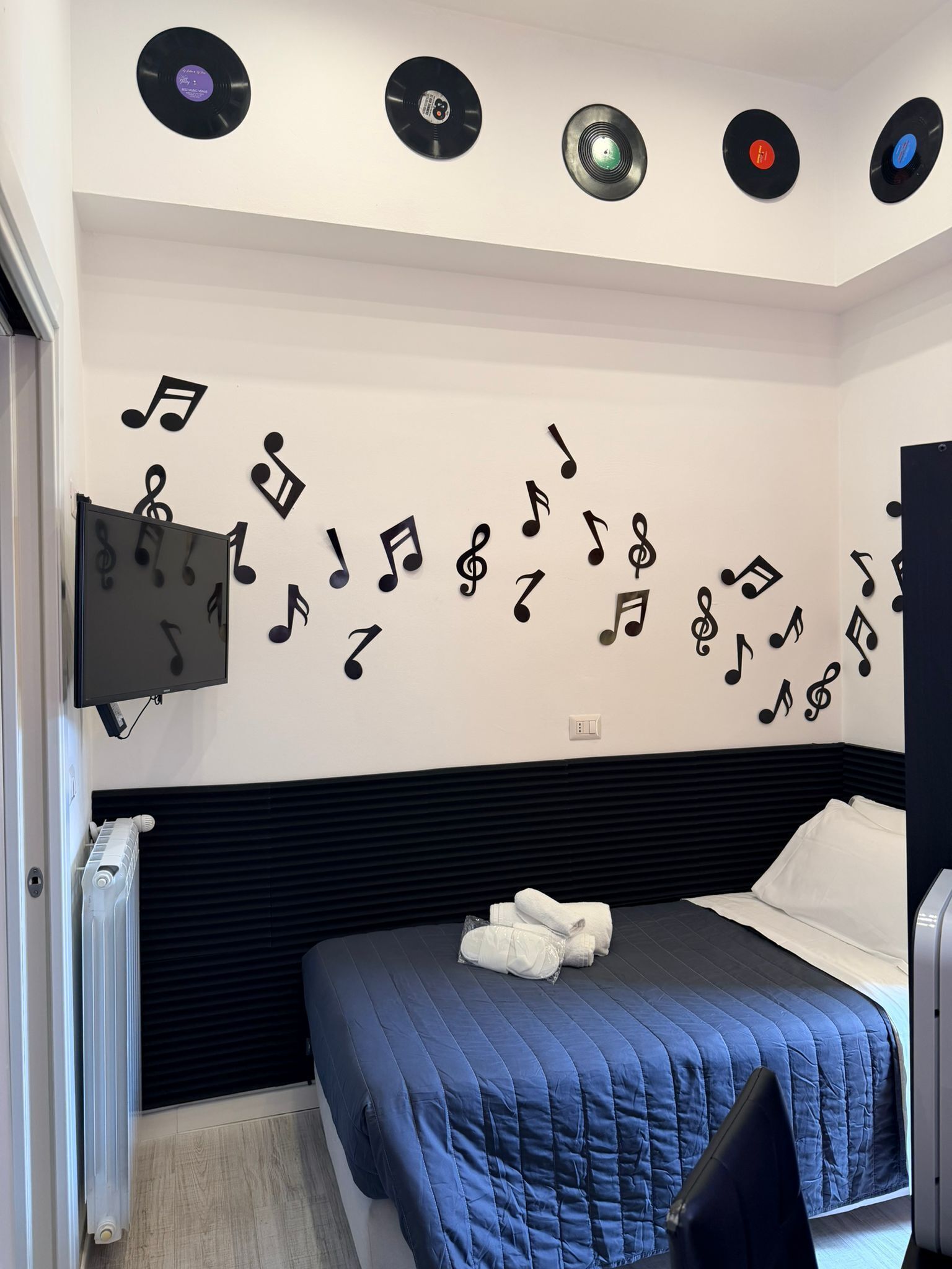 Ein Schlafzimmer mit einem Bett, einem Flachbildfernseher und Wanddekorationen, darunter Schallplatten und Noten.