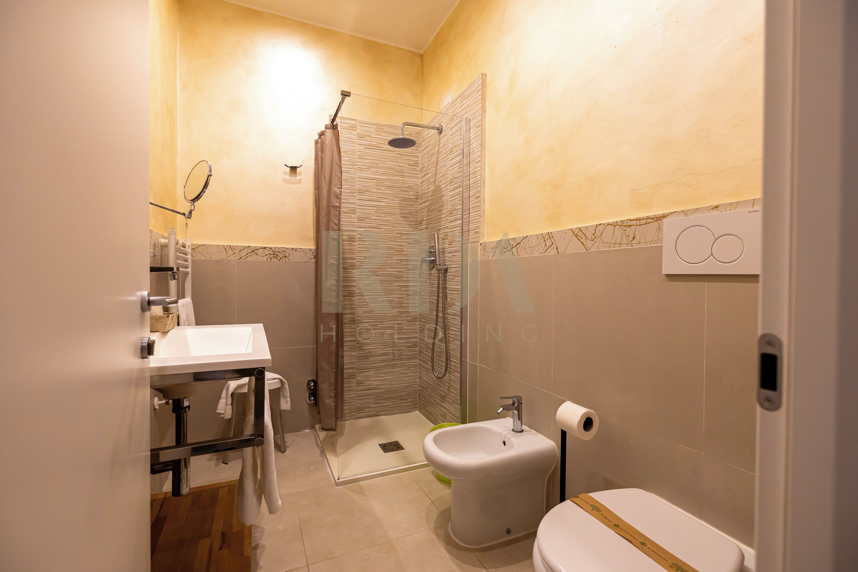 Un baño con ducha, inodoro, lavamanos y toallero.